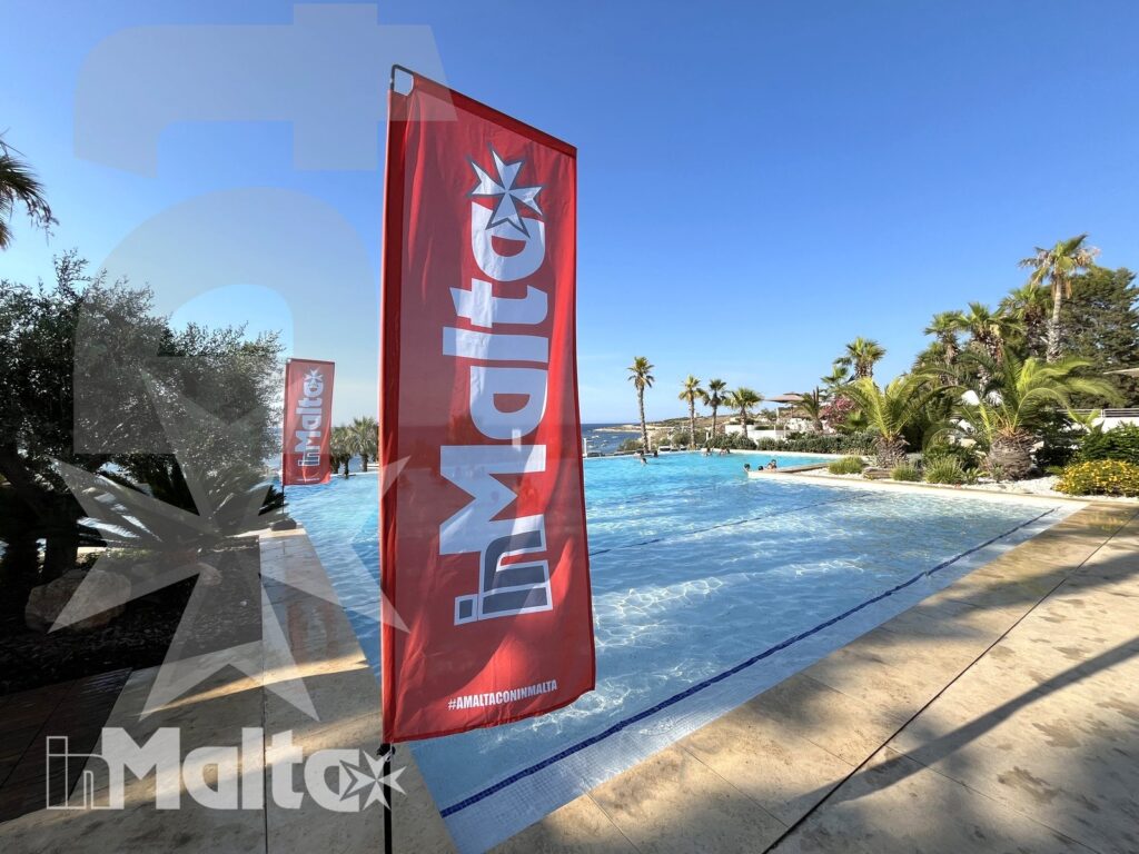 Piscina del resort e giardino mediterraneo Piscina esterna luminosa con acqua turchese, bandiera promozionale rossa, palme e giardino curato.