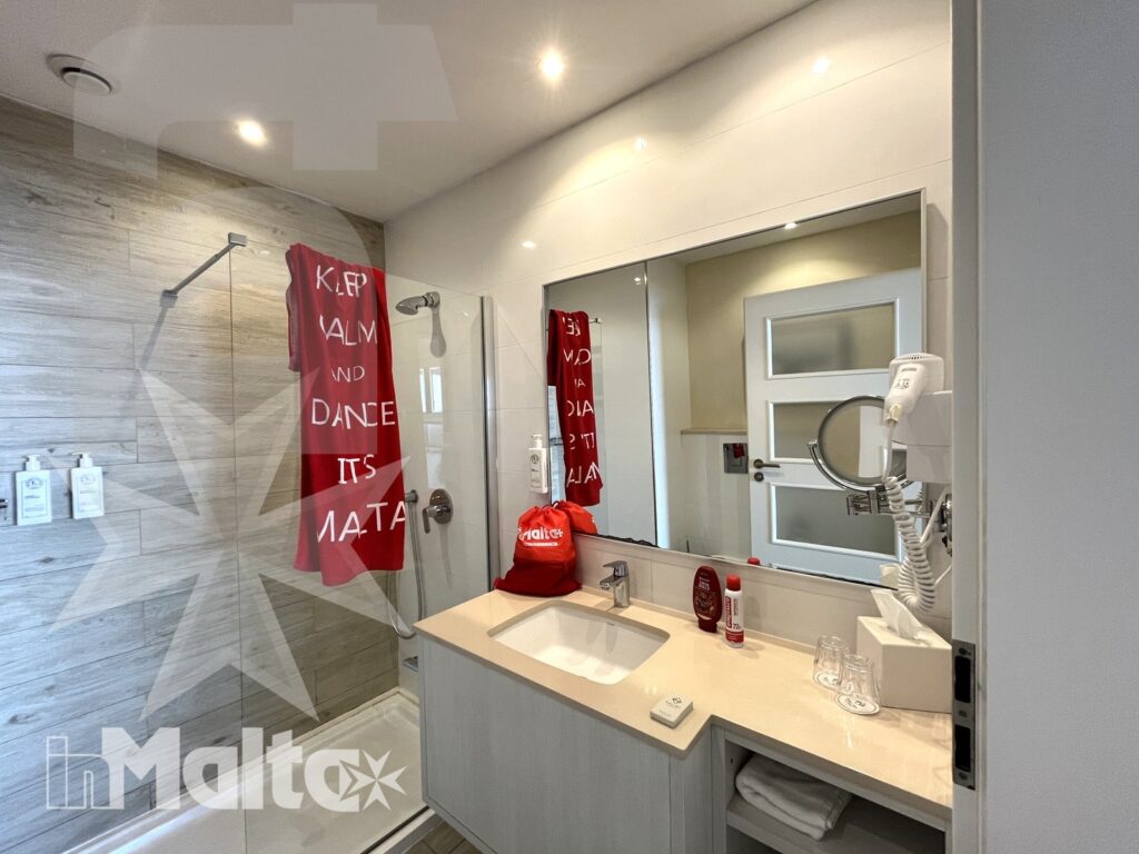 Bagno moderno con doccia, lavabo, specchio, asciugamani e accessori per gli ospiti della struttura ricettiva a Malta.