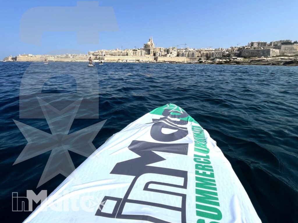 Vista dalla tavola da stand up paddle verso la costa fortificata di Malta, con mare blu intenso e cielo sereno.