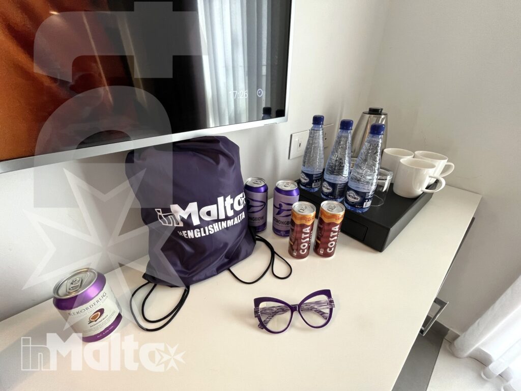 Omaggi e bevande di benvenuto nella camera a Malta Omaggi, bottiglie d'acqua, bevande e tazze disposti sulla scrivania della camera, un'accoglienza curata per giovani ospiti a Malta.
