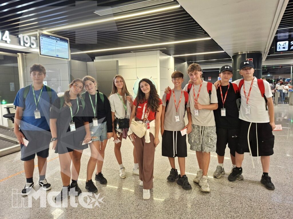 Partecipanti in aeroporto all'inizio del viaggio verso Malta Gruppo internazionale di studenti con badge posa nell'area partenze di un aeroporto, pronto a iniziare il viaggio verso Malta.
