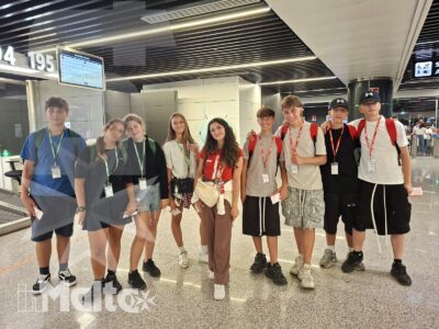 Gruppo internazionale di studenti con badge posa nell'area partenze di un aeroporto, pronto a iniziare il viaggio verso Malta.