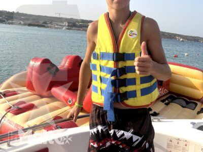 Uno studente sorridente mostra il pollice alzato a bordo di un gommone, indossando il giubbotto salvagente durante l'attività nautica.