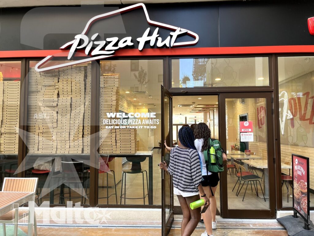 Due studenti entrano in un ristorante Pizza Hut, riconoscibile dall'insegna e dalle vetrine d'ingresso.
