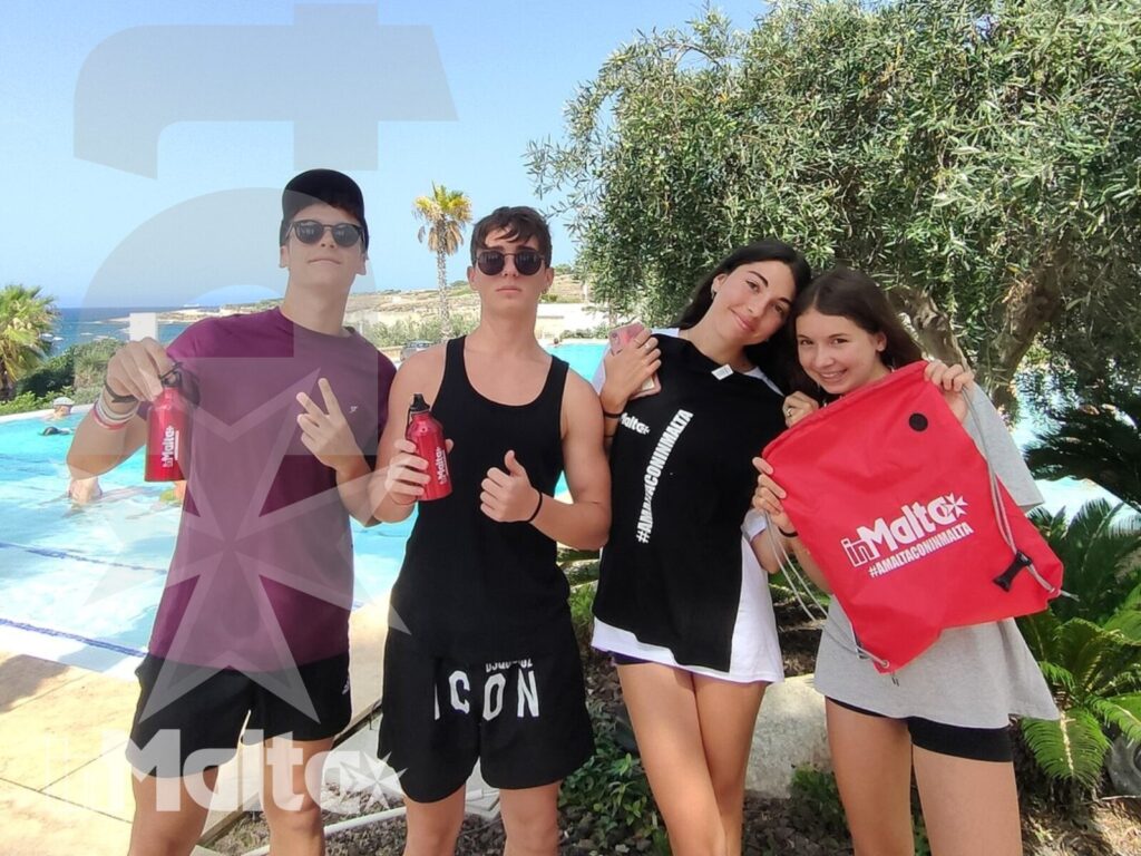 Partecipanti alle vacanze studio posano vicino alla piscina Quattro studenti sorridenti posano a bordo piscina con il mare sullo sfondo, vivendo un momento di socialità durante le vacanze studio.