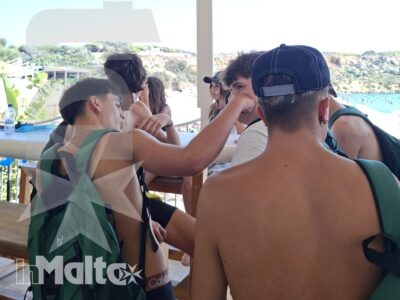 Gruppo di studenti con zaini conversa su una terrazza panoramica affacciata sul mare, durante un'escursione di gruppo a Malta.