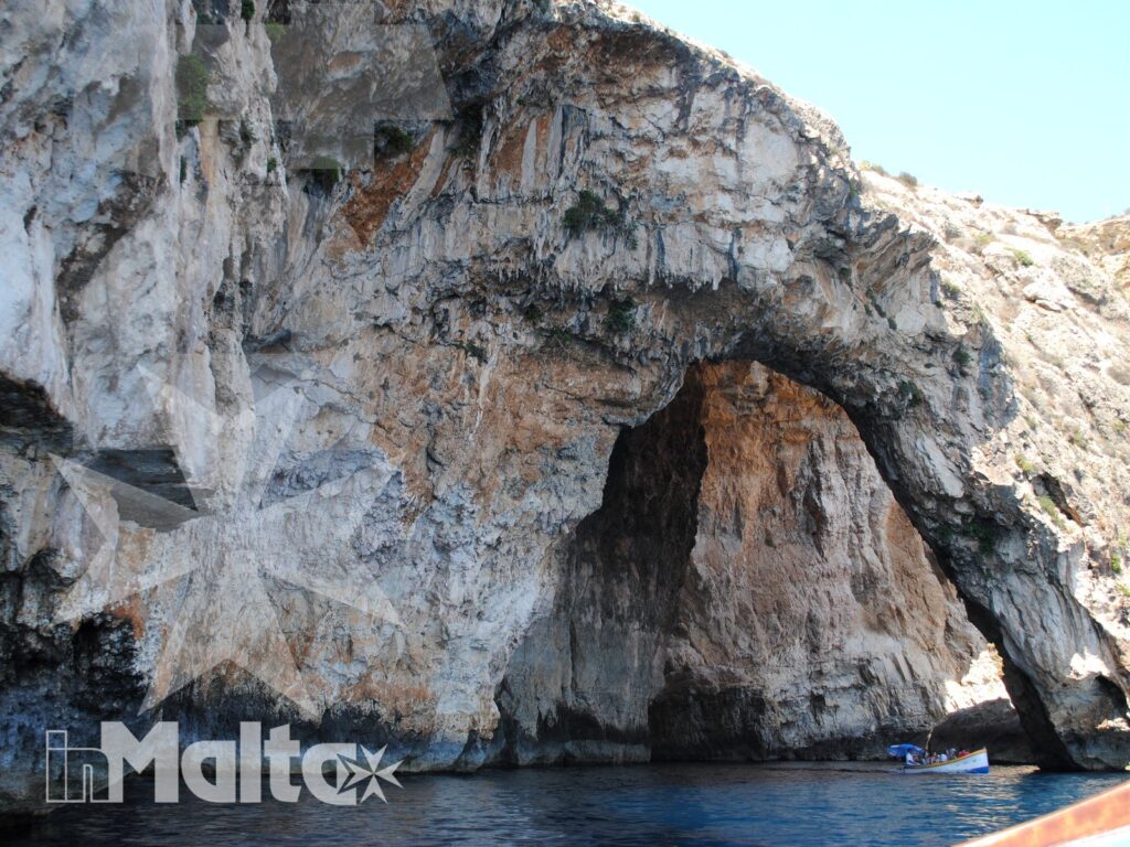L'ampio arco della scogliera calcarea emerge dall'acqua blu, osservato dal mare durante una gita in barca alla Blue Grotto.