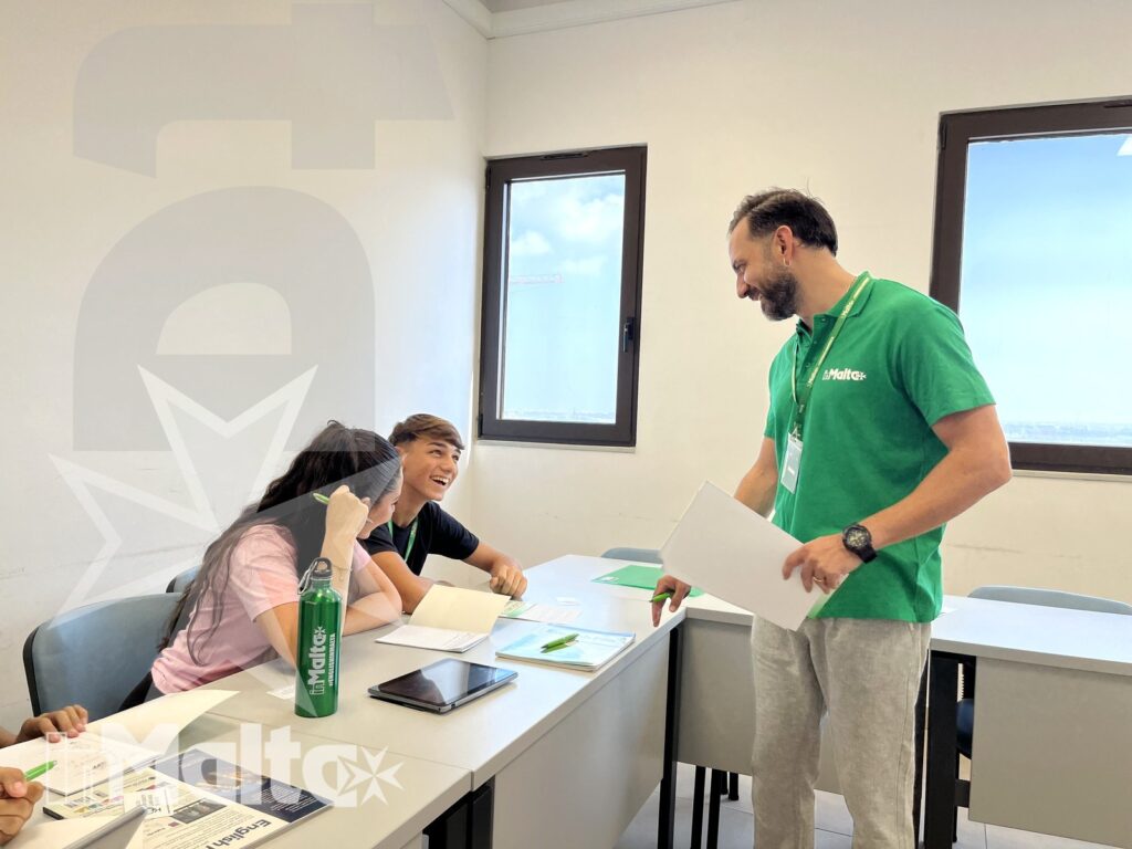 Tutor e studenti durante una lezione partecipativa Tutor in piedi interagisce con studenti seduti ai banchi, tra quaderni, tablet e materiali scolastici.