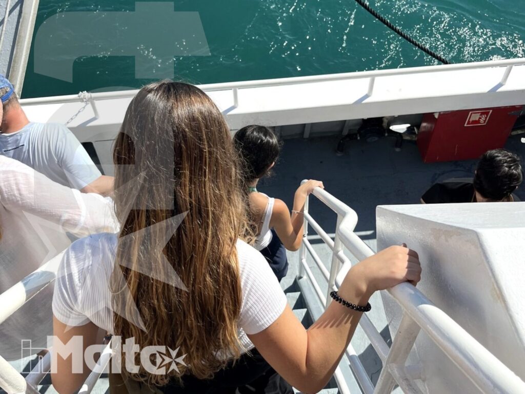 Studenti scendono la scaletta di una barca nelle acque turchesi di Malta, ripresi dall'alto durante un'attività sul mare.