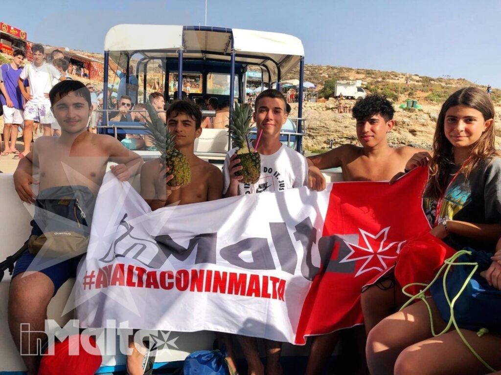 Studenti inMalta sul trenino turistico durante l'escursione Gruppo di studenti sorride sul trenino turistico mostrando bandiere, con il paesaggio maltese sullo sfondo.