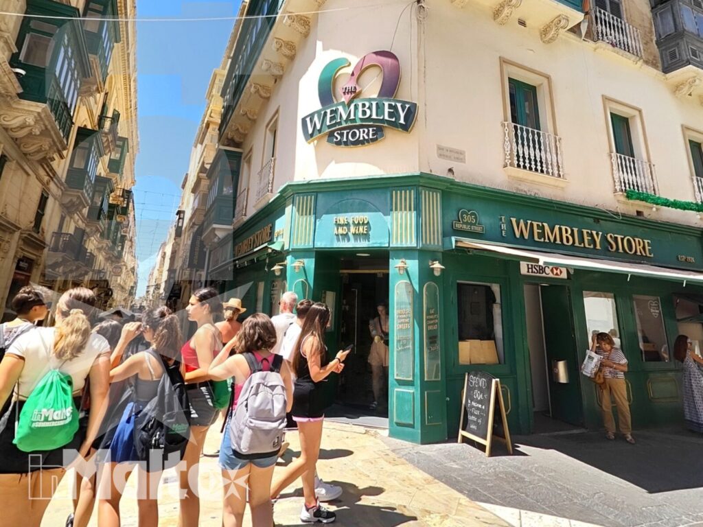 Gruppo di studenti visita un caratteristico negozio maltese lungo una strada storica del centro, illuminata dal sole.