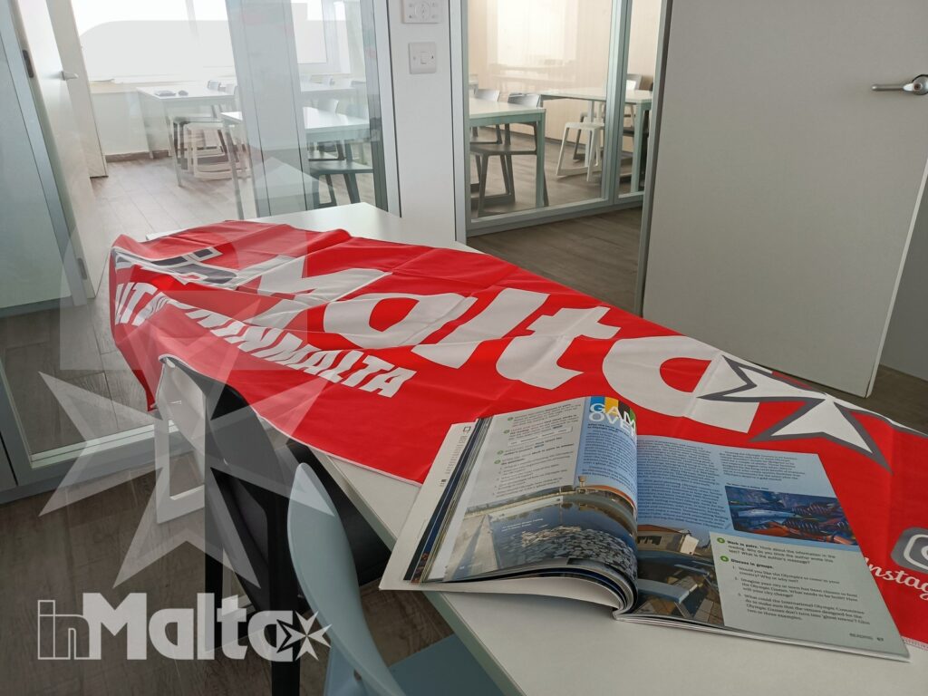 Tavolo da studio con rivista turistica aperta e bandiera rossa decorativa in un ambiente interno luminoso e vetrato.