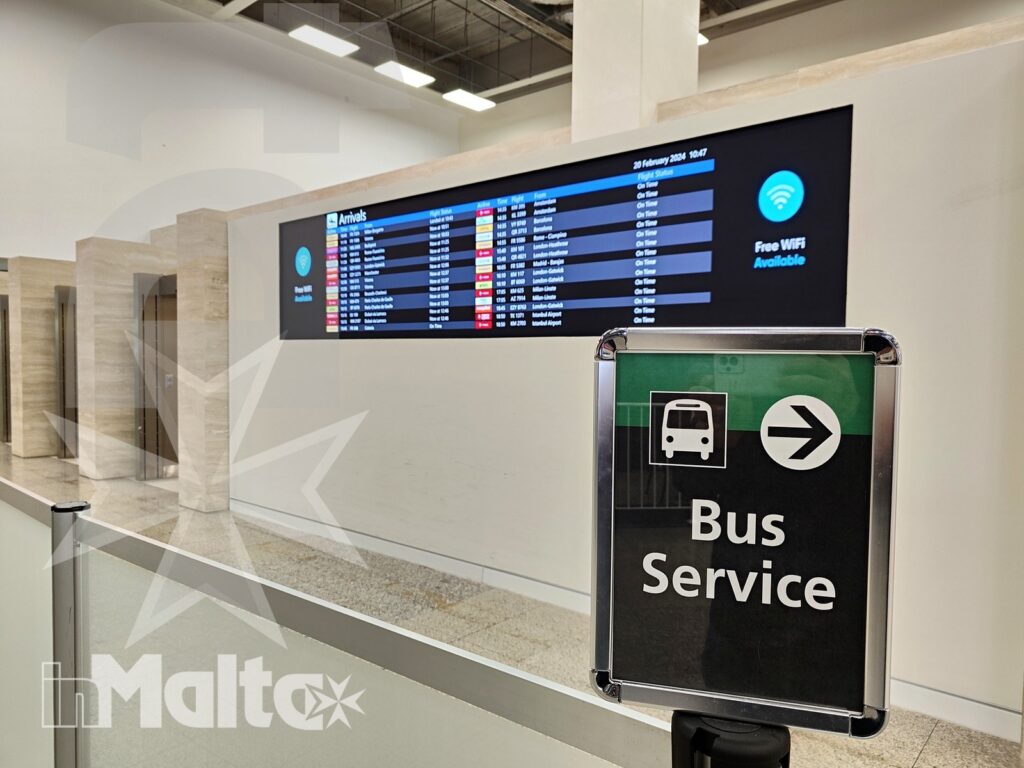 Indicazioni per autobus e arrivi all'aeroporto di Malta Cartello per il servizio autobus davanti al tabellone degli arrivi nell'aeroporto di Malta, con indicazioni chiare per i viaggiatori.