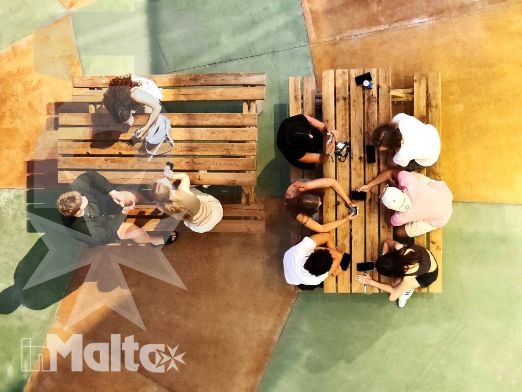 Studenti seduti attorno a tavoli di legno durante un'attività condivisa, in una piazza colorata del Campus Hub per il soggiorno studio.