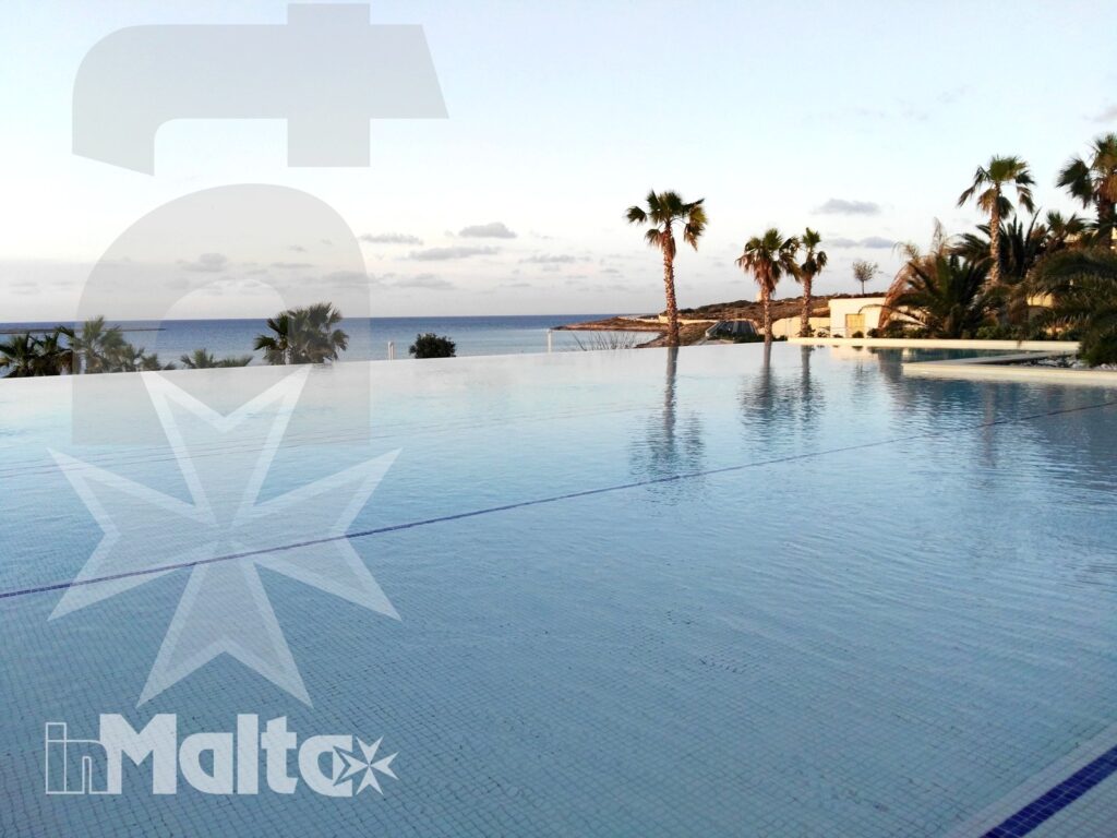 Piscina a sfioro vuota illuminata dal tramonto, con palme in controluce e orizzonte marino aperto.