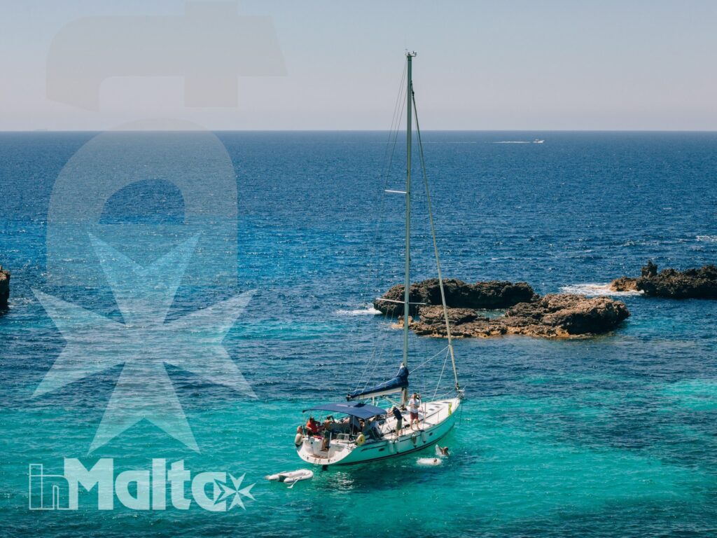 Barca a vela con persone a bordo naviga sulle acque turchesi di Malta, davanti a una costa rocciosa.