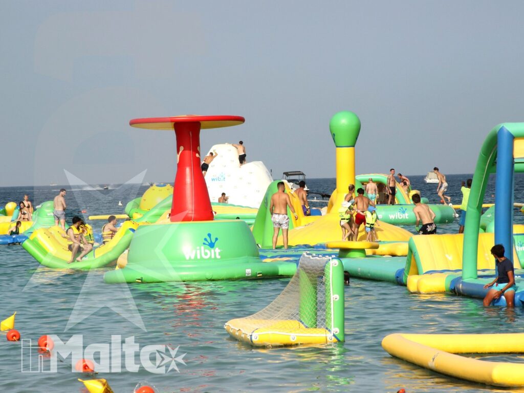 Parco acquatico galleggiante per gruppi e famiglie a Malta Ampio parco giochi gonfiabile in mare, affollato da bambini, adolescenti e adulti che scivolano, si arrampicano e giocano.
