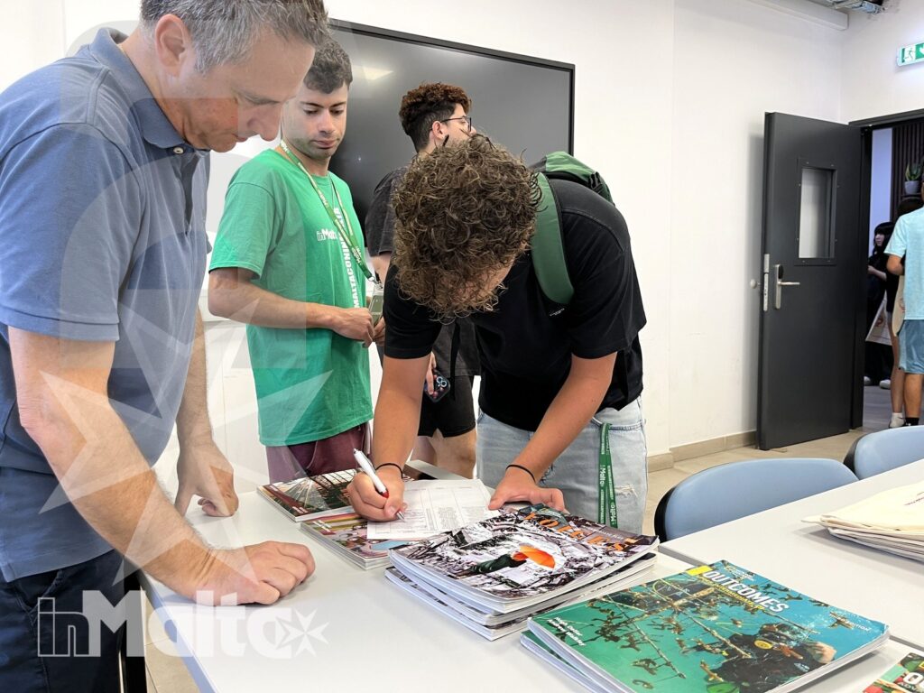 Studenti collaborano sui materiali del programma scolastico Studenti e accompagnatore compilano moduli e consultano riviste attorno a un tavolo durante un'attività organizzativa.