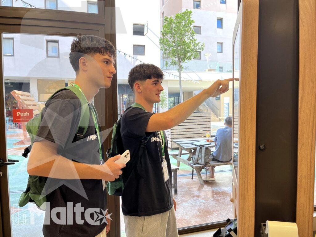 Due studenti con zaini indicano l'ingresso di una struttura urbana, pronti a orientarsi durante la vacanza studio.