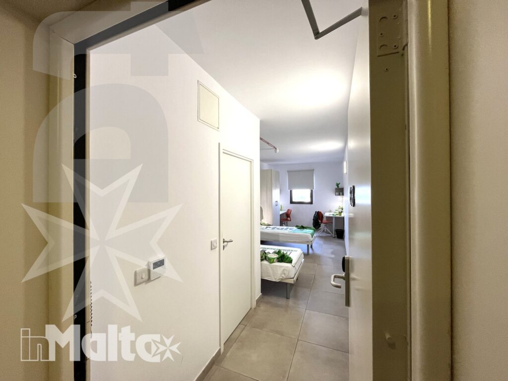 Ingresso della camera doppia del Campus inMalta con armadi e letti