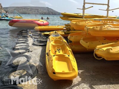 Kayak gialli e gommoni colorati sono raccolti sulla riva di una baia, pronti per un'attività acquatica.