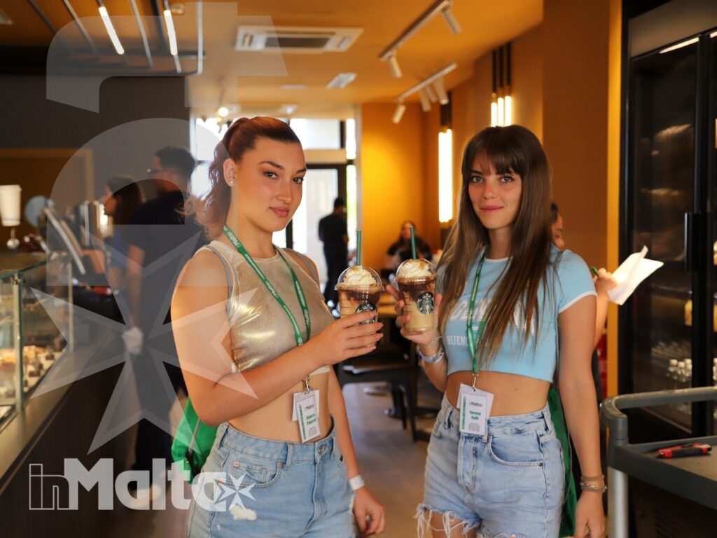 Due studentesse sorridono mostrando bevande fredde in una caffetteria moderna, durante una pausa del soggiorno linguistico.