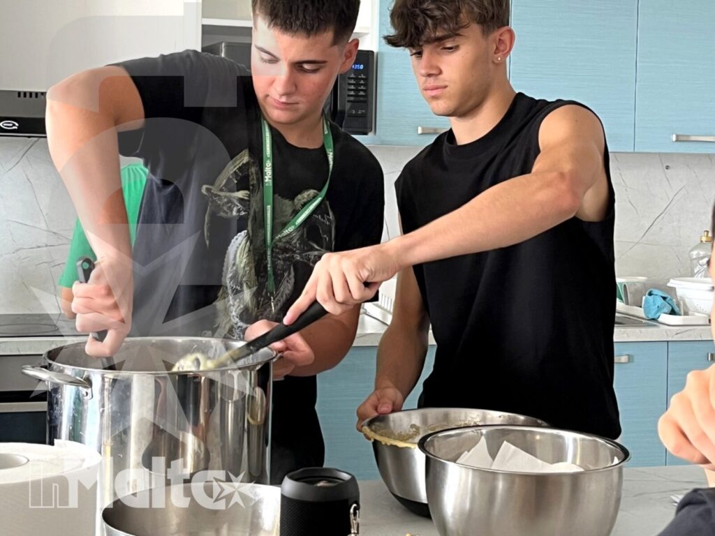 Due studenti collaborano ai fornelli tra pentole, ciotole e utensili durante un laboratorio di cucina condiviso nel campus.