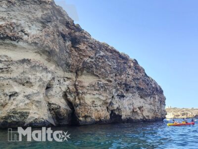 Imponente scogliera calcarea si affaccia sull'acqua turchese, con piccole barche sullo sfondo durante un'escursione lungo la costa di Malta.
