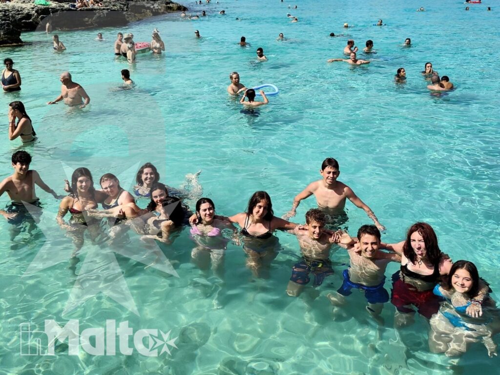 Studenti nella baia durante il soggiorno a Malta Gruppo di studenti sorride nell'acqua cristallina davanti alla baia rocciosa, durante un'attività balneare a Malta.