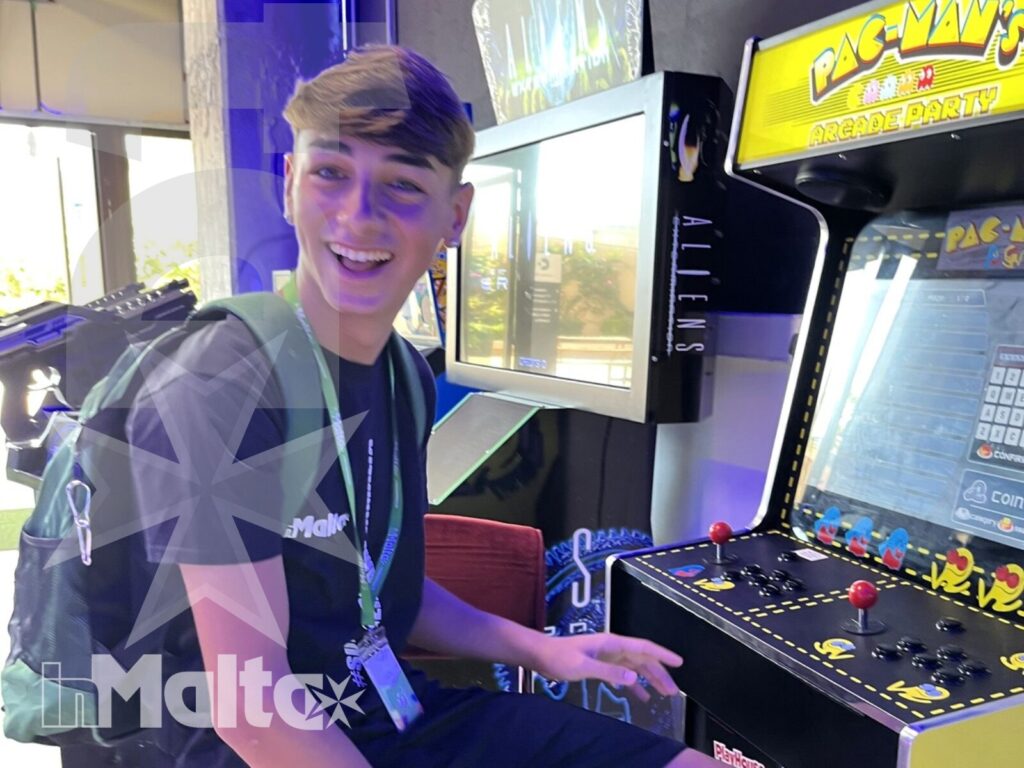 Uno studente sorridente gioca a Pac-Man in una sala giochi interna durante il soggiorno a Malta.