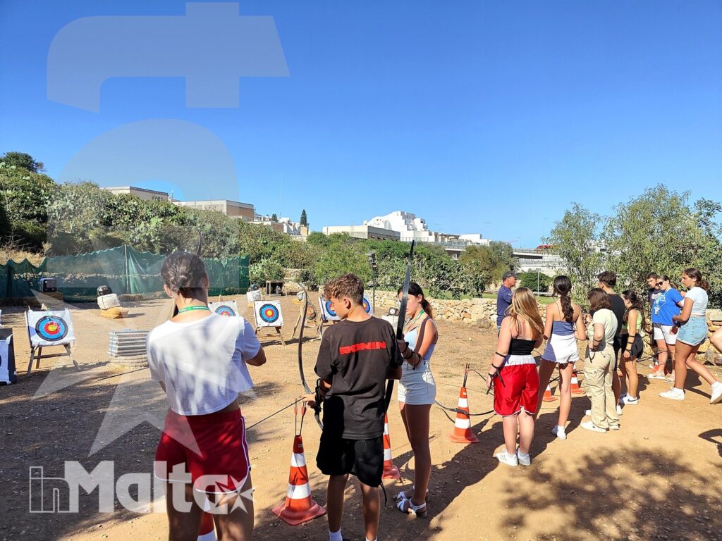 Partecipanti osservano e praticano il tiro con l'arco in un'area mediterranea delimitata da coni, durante una giornata a Malta.