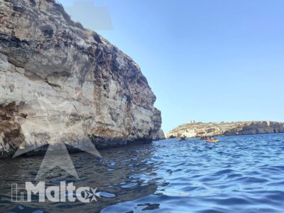 Una scogliera calcarea domina il mare blu, ripresa dal livello dell'acqua durante una possibile gita costiera.