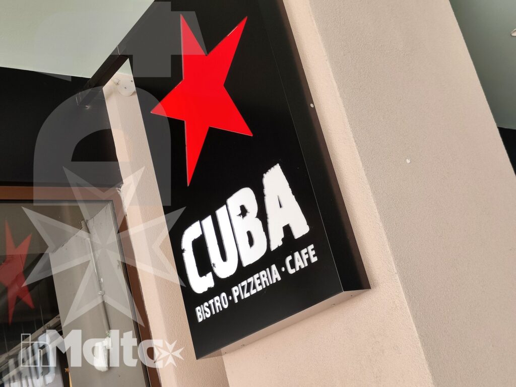 Insegna verticale con logo rosso e nome Cuba Bistro-Pizzeria-Café, ripresa dal basso all'ingresso del locale del Campus Hub.