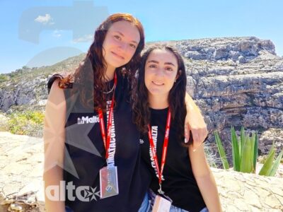 Due studentesse sorridenti e abbracciate posano davanti alle scogliere calcaree durante un soggiorno studio a Malta.
